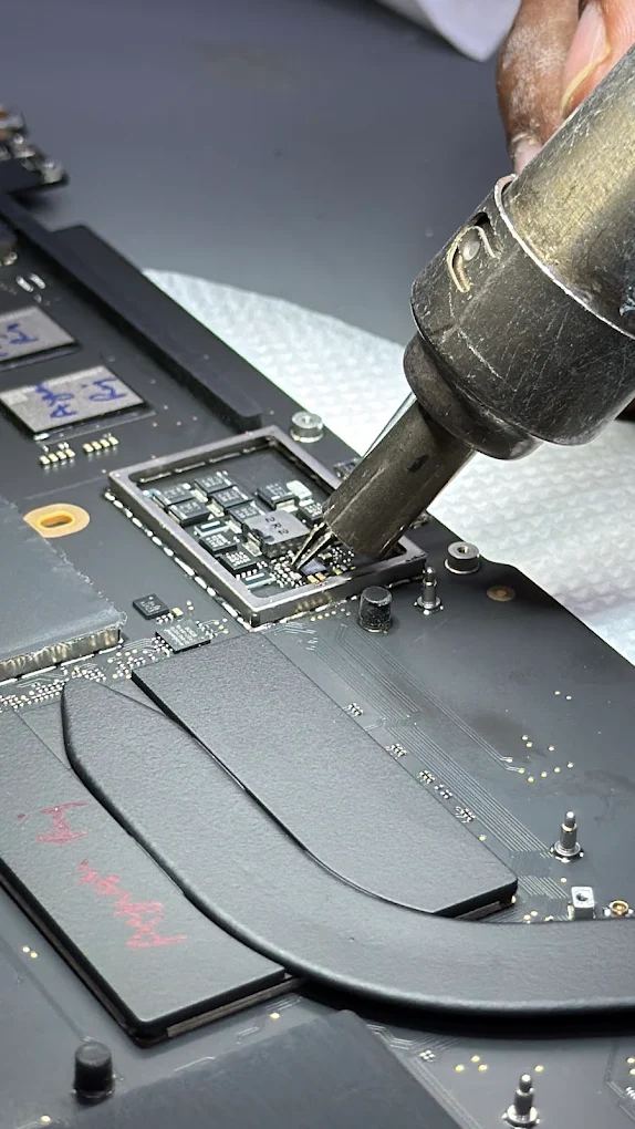 Hot-air rework station lifting an integrated circuit from a MacBook logic board with the shield removed