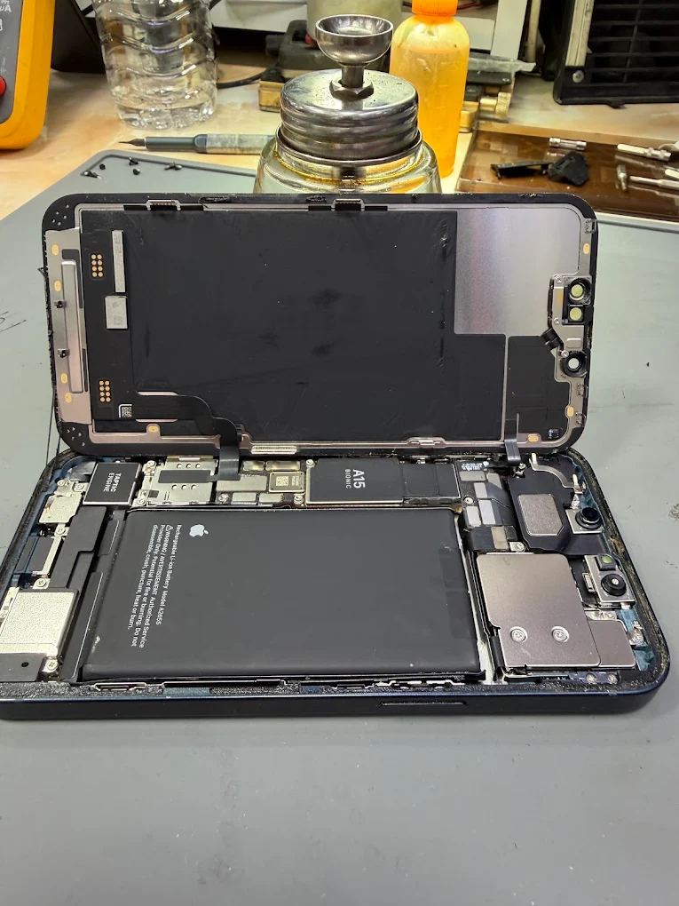 An iPhone opened on the bench with the display, battery and logic board exposed