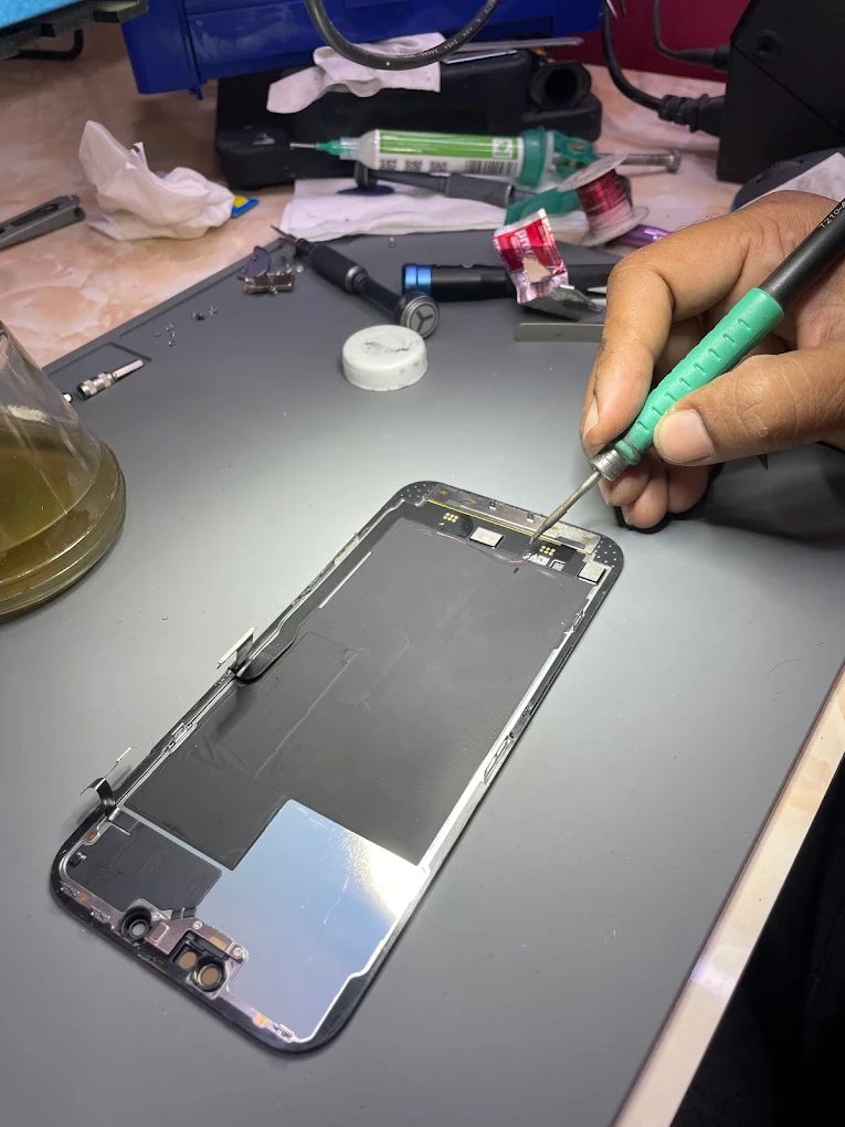 A soldering iron working on the display assembly of an iPhone laid face-down on the mat