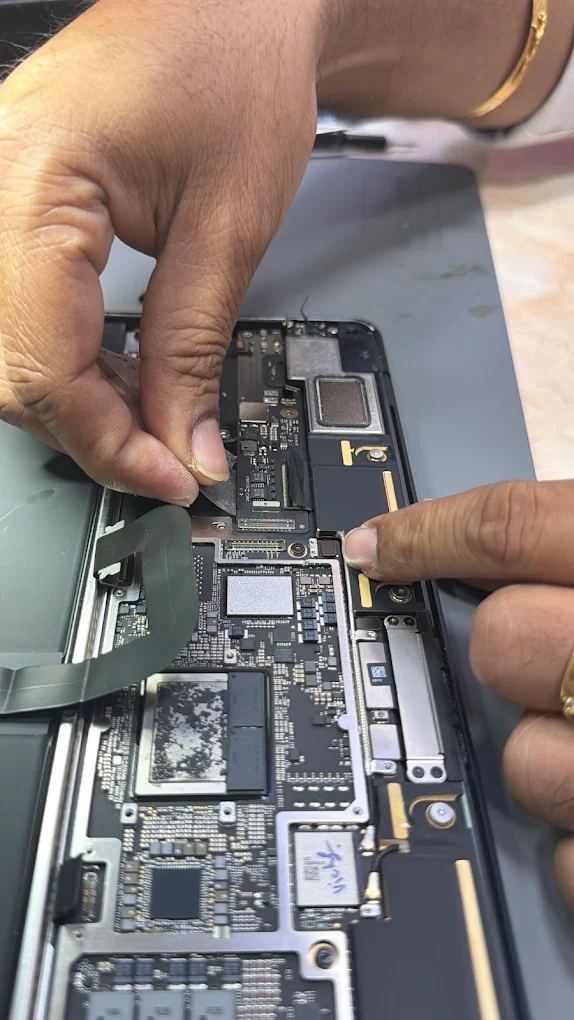 Technician reseating display and board flex cables inside an opened MacBook