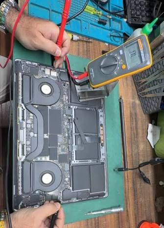 A 16-inch MacBook Pro opened up, its board being measured with a Fluke multimeter