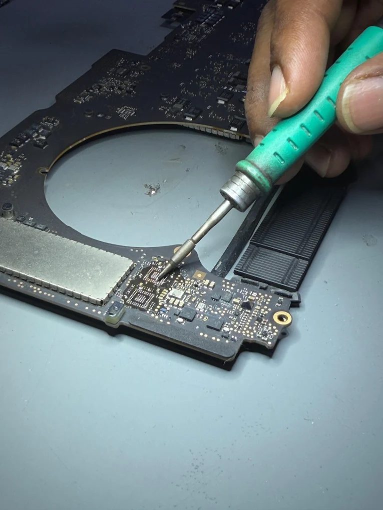 A soldering iron working on a small component on a MacBook logic board