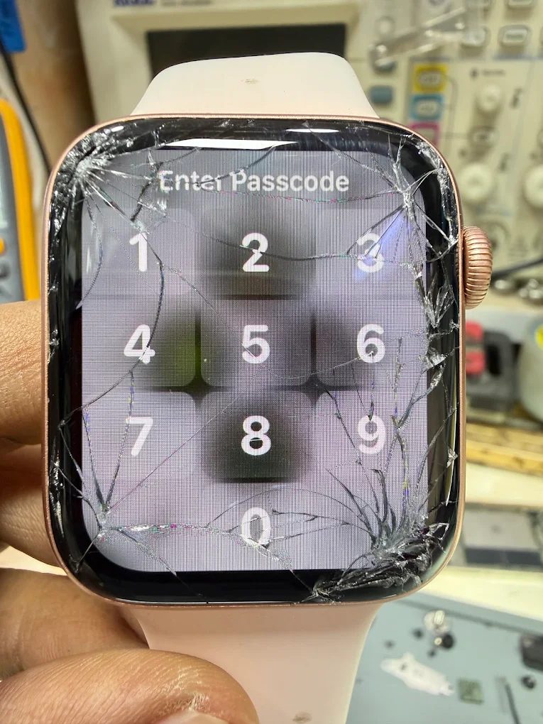 An Apple Watch with shattered front glass still showing its passcode screen